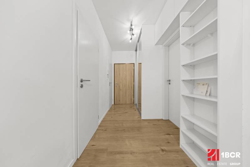 Hallway of a 2-room apartment with a wooden decor floor and white walls.