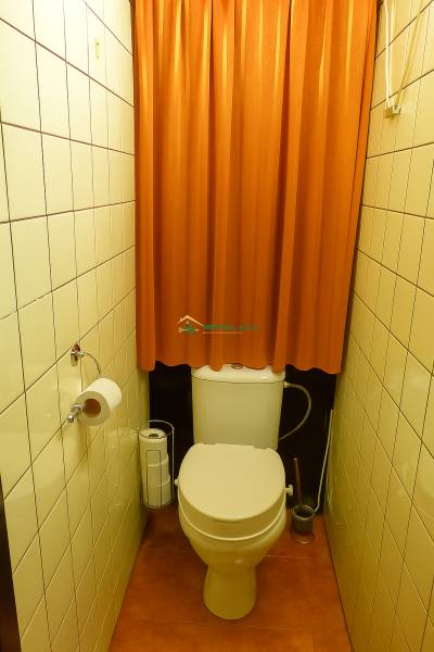 A toilet with an orange curtain and light tiles in a 2-room apartment.