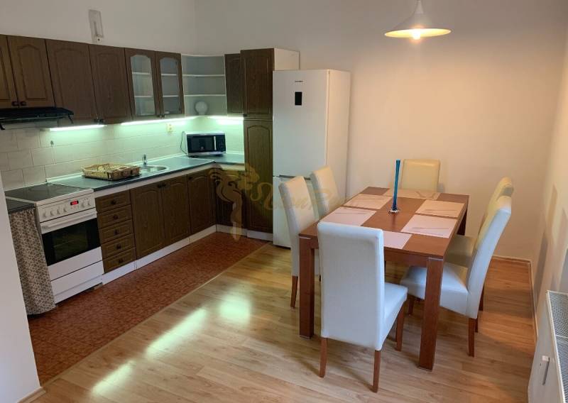A kitchen in a 2-room apartment with a table, wooden cabinets, and a floor with a wood decor.
