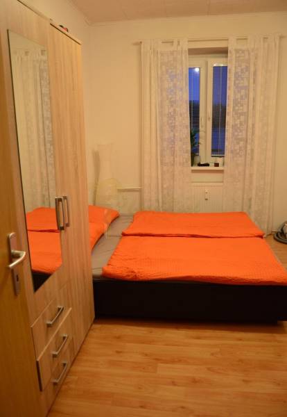 Bedroom in a two-room apartment with orange bedding and a wooden decor floor.