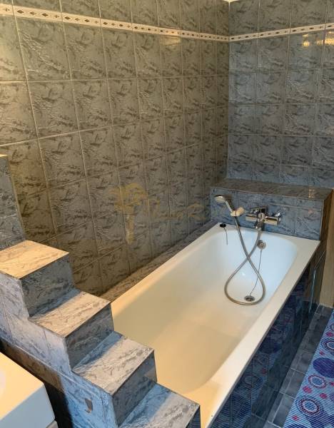 A bathroom in a 2-room apartment with a bathtub and marble tile cladding.