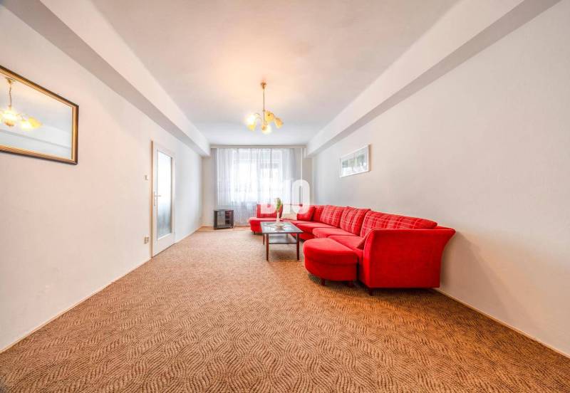 Living room with a light wall, red sofa, and carpet in a 4-room apartment.