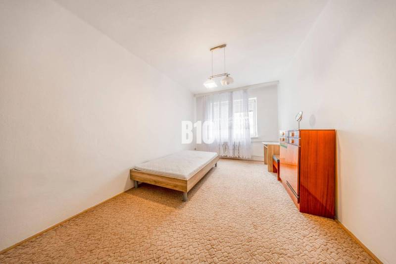 A bedroom in a 4-room apartment with a bed, a dresser, and a carpet.