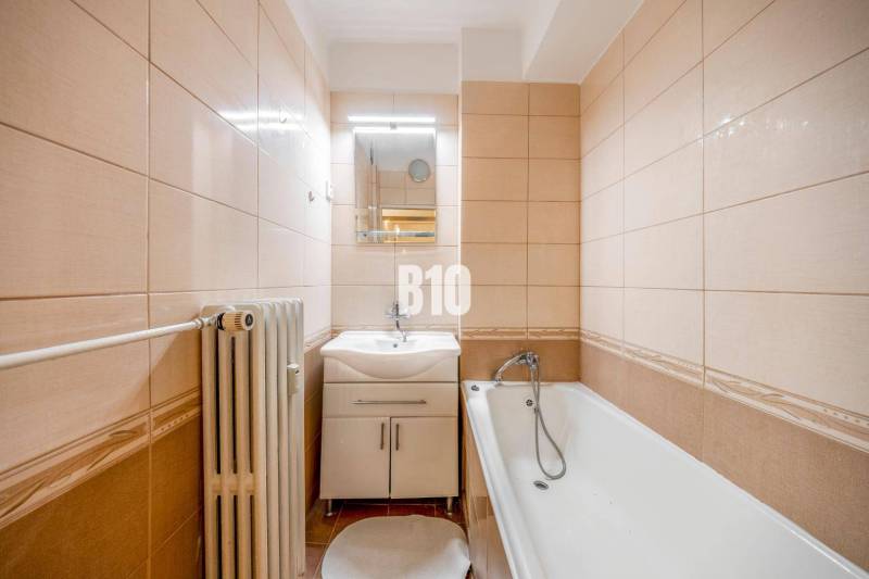 A bathroom in a 4-room apartment with a bathtub, light tiles, and a radiator.