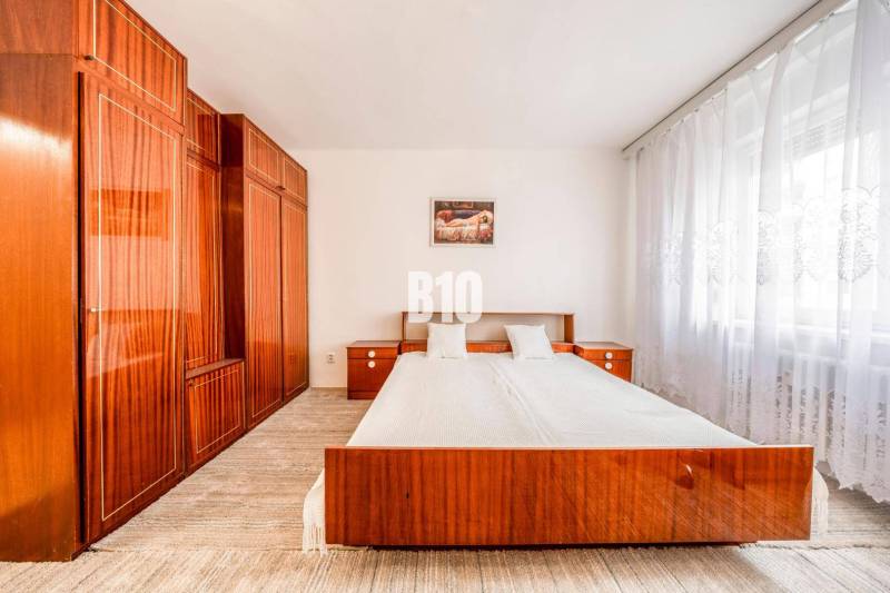 Bedroom in a 4-room apartment with a double bed and built-in wardrobes, light curtains.