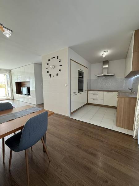 Dining area in a 4-room apartment with a wood-patterned floor and a kitchen in the background.