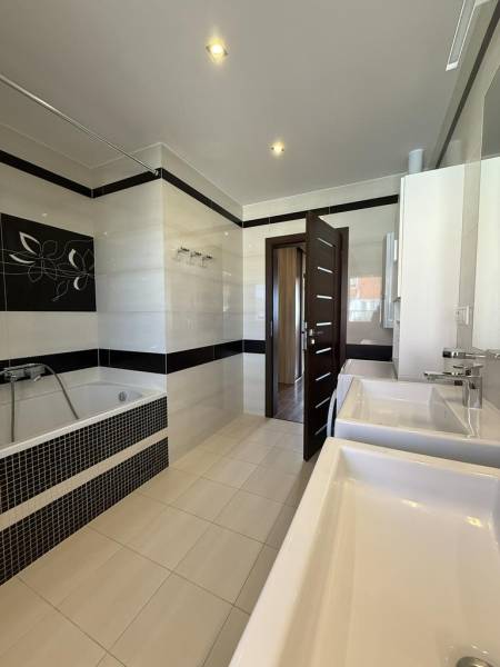 A bathroom in a 4-room apartment with two sinks, a bathtub, and tiles.