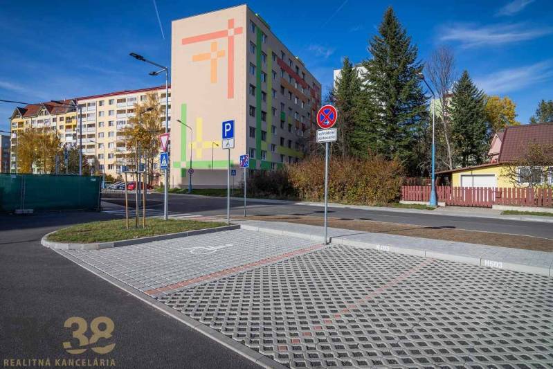 Exterior with an apartment building and a parking lot in Poprad, greenery and houses in the background.