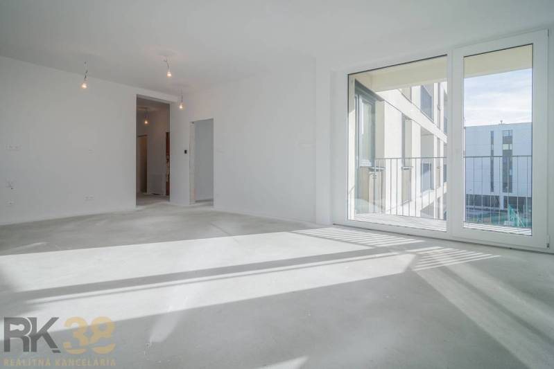 A room in a 3-room apartment with a large window, wooden decor flooring, white walls.