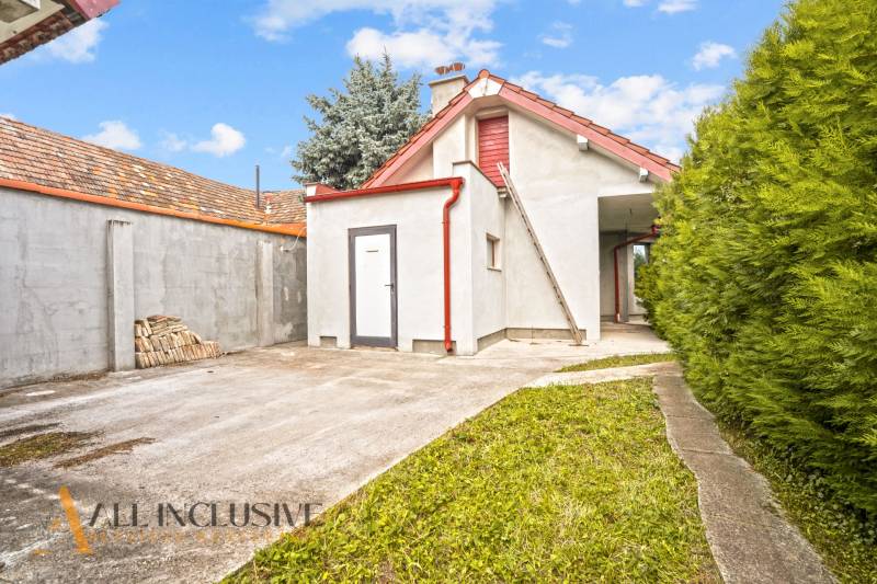 A family house in Bátorove Kosihy with a one-story extension, a gravel road, and coniferous trees.