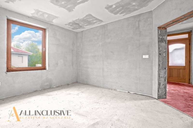 Unfinished room in a family house with a concrete floor and a large window.
