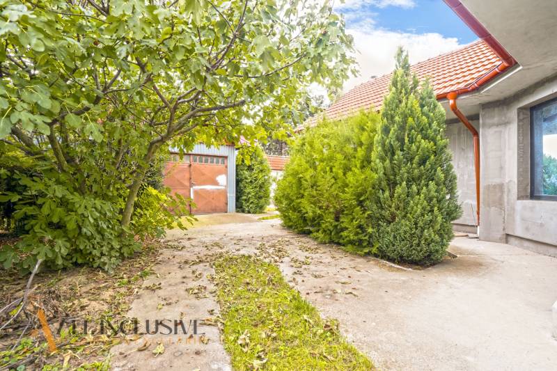 A family house in Bátorove Kosihy with a lush garden and a metal garage door.