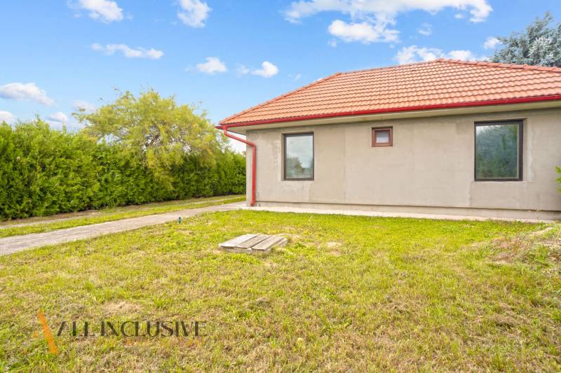 A family house in Bátorove Kosihy with a red roof surrounded by green lawn and shrubs.