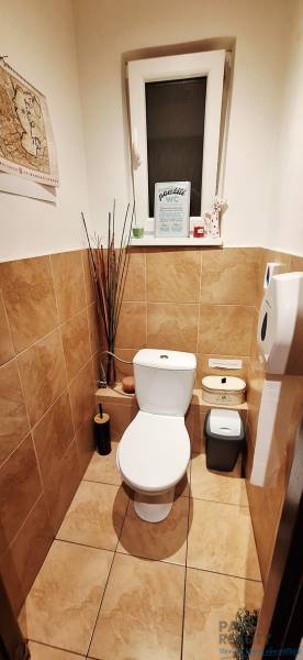 Small bathroom with toilet, accessories on the shelf, white sanitary ware, tiles with stone decor.