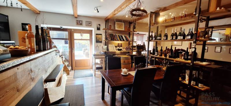 Interior of commercial space with a bar, table, and wine shelves, floor with wooden decor.
