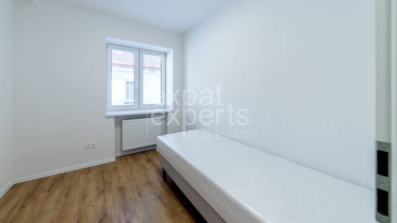 A room with a single bed, a window, and a floor with a wooden decor in a 3-room apartment.