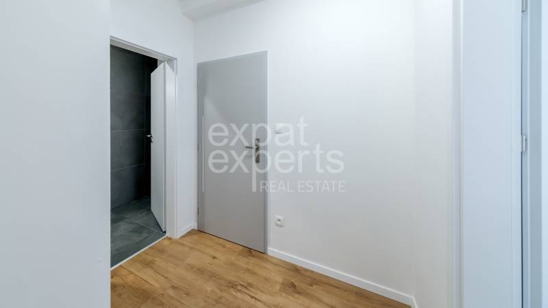 A hallway with gray doors, a bathroom with dark tiles, and a floor with a wooden decor.