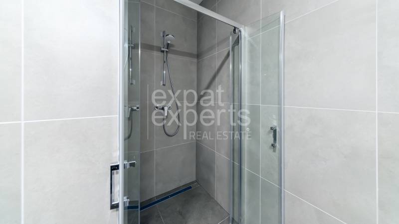 Shower corner with transparent doors and gray tiles in a 3-room apartment.