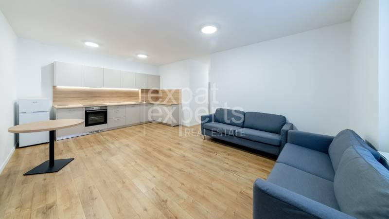 Kitchen and living room in a 3-room apartment with a wooden decor floor, gray sofas, and a table.