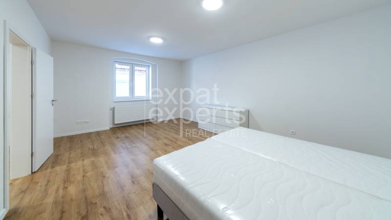 A bright bedroom with wood-patterned flooring, a bed, and a window in a three-room apartment.