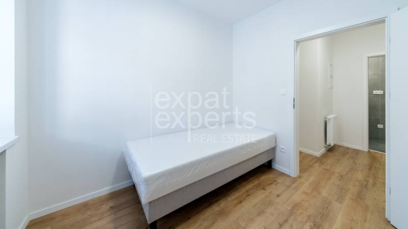 A simple room in a 3-room apartment with a bed and a wooden floor decor.