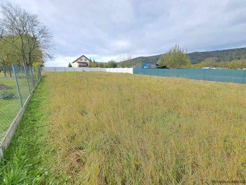 A plot of land with grass, trees, suitable for living, fenced, house in the background.