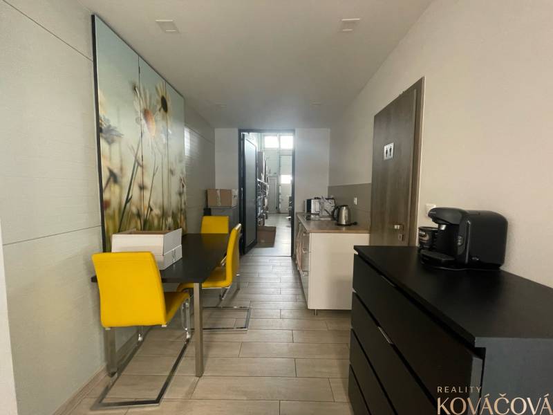 Commercial space with a dining table, yellow chairs, and a kitchenette.