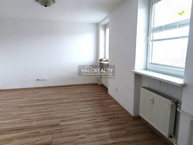 A bright room with wood-patterned flooring in a studio apartment and a large window.