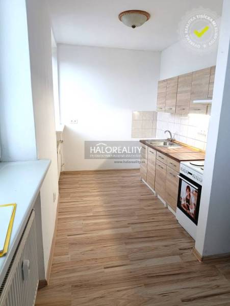 The kitchen of a one-room apartment with a kitchen unit on a floor with a wooden decor.