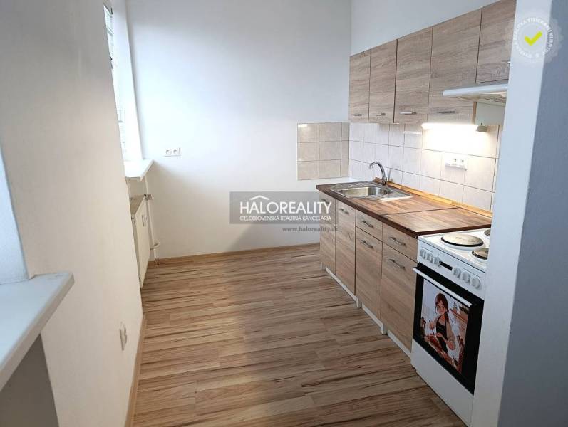 A kitchen in a studio apartment with a kitchenette and a stove, flooring with a wooden decor.