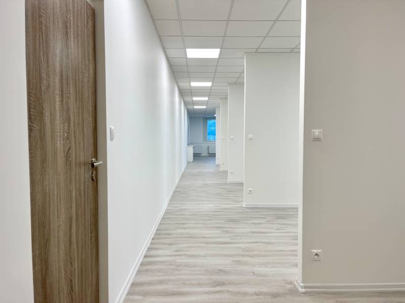 A hallway in an office with white walls, lights, and a wooden decor floor.