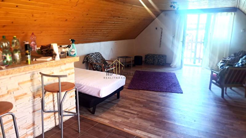 The interior of a cabin with a bar counter, bed, and wooden decor flooring.