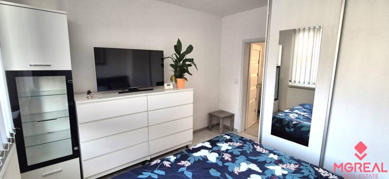 Bedroom in a 2-room apartment with white furniture, a mirror, and a TV on the dresser.