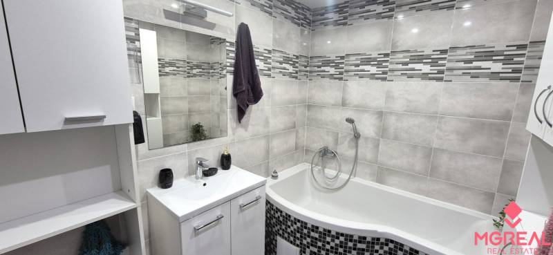 A bathroom in a 2-room apartment with a corner bathtub and gray tiles.