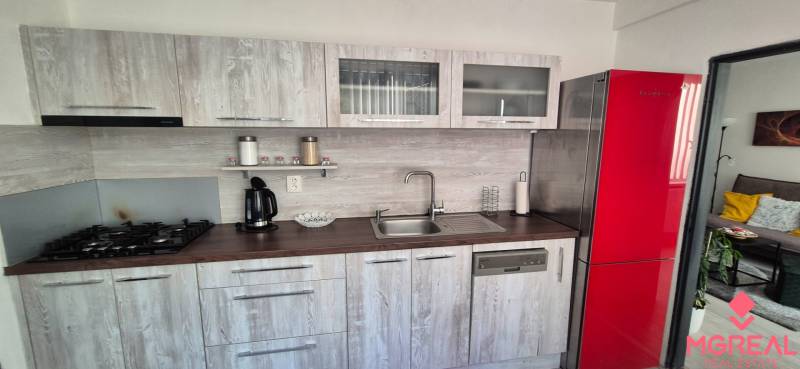 A kitchen in a 2-room apartment with a red refrigerator and a wooden-patterned floor.