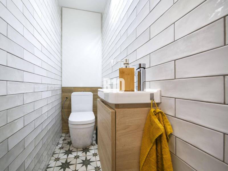 A narrow bathroom with tiles, a toilet, and a sink in a 3-room apartment.