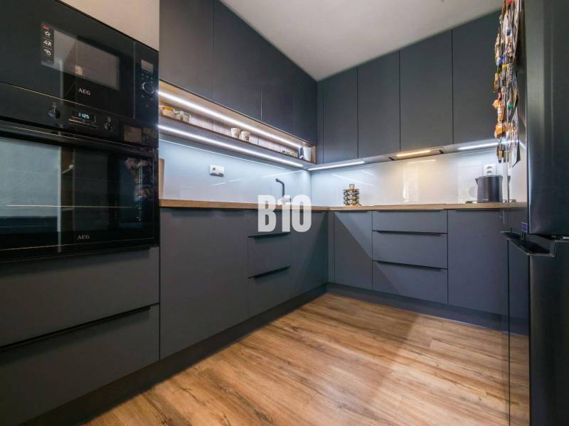A kitchen in a 3-room apartment with dark cabinets and a wooden-patterned floor.