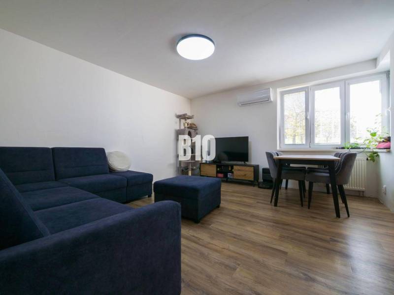 Living room in a three-room apartment with a sofa, television, and wooden decor flooring.