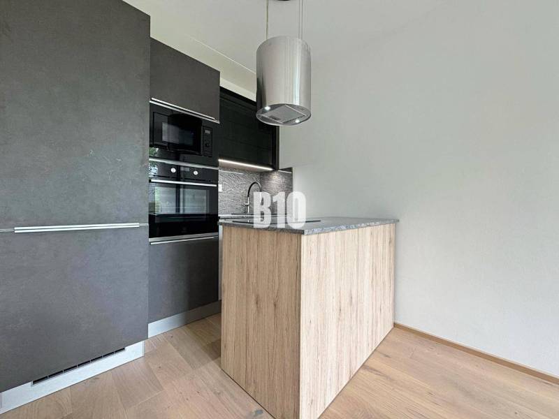 A modern kitchen in a 2-room apartment with wooden flooring and a dark cabinet.