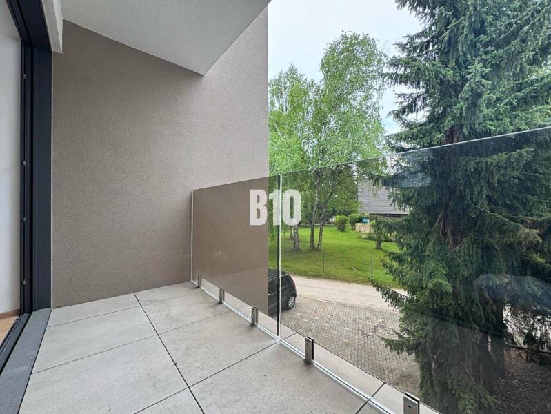 A balcony with glass railings offering a view of greenery in a 2-room apartment.