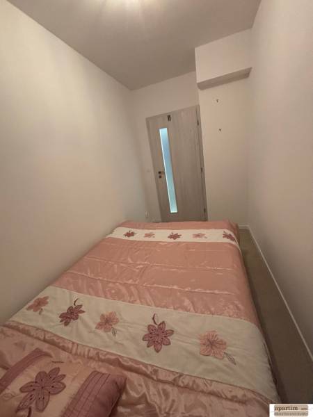 A bedroom in a 2-room apartment with a bed featuring a floral motif and light-colored walls.