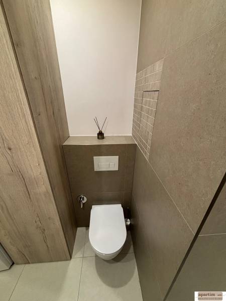 A toilet in a 2-room apartment with tiles and a wooden decor on the wall.