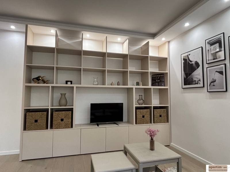 A storage wall with shelves and decorations in a 2-room apartment, next to a table with flowers.
