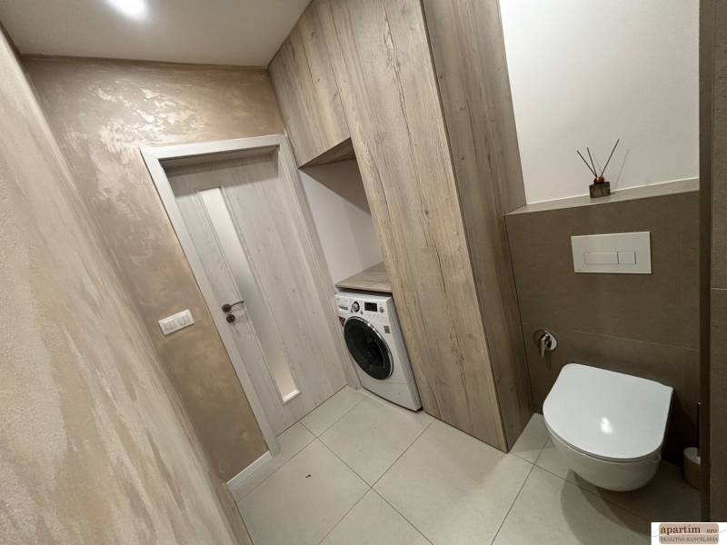 Bathroom in a 2-room apartment with a toilet and a washing machine, floor with wooden decor.