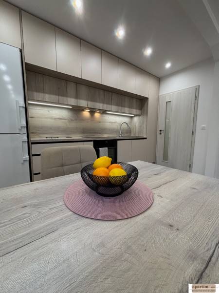 A kitchen with light cabinets and a bowl of fruit on a wooden table in a 2-room apartment.
