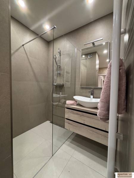 Bathroom with a shower, sink on a cabinet, and mirror in a 2-room apartment.