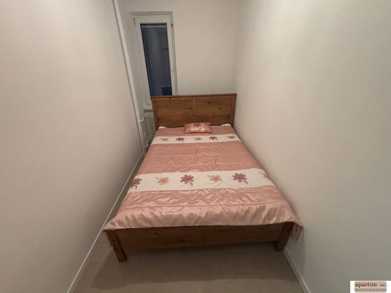 A narrow bedroom in a two-room apartment with a wooden bed and a floral bedspread.