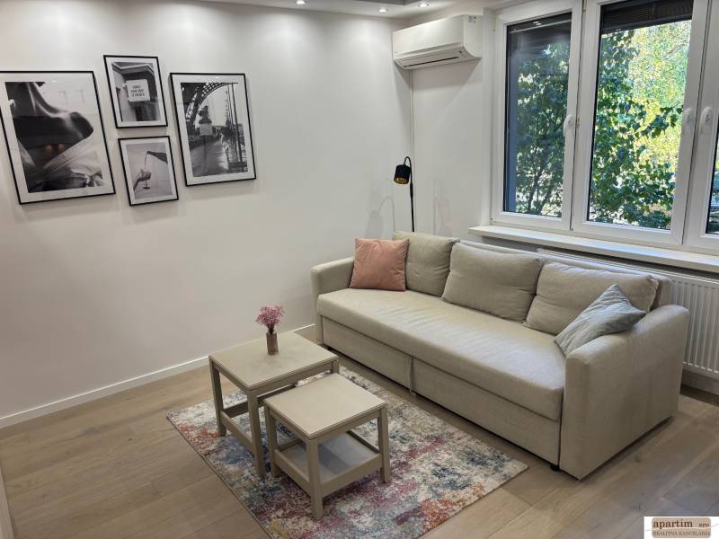 Living room in a 2-room apartment, with a sofa, tables, and photographs on the wall.