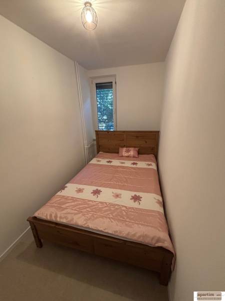 A narrow bedroom with a bed with a patterned pink blanket in a two-room apartment.