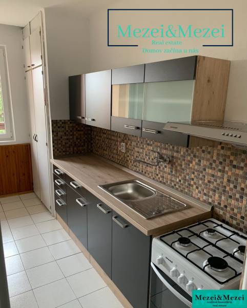 A kitchen in a 2-room apartment with dark furniture and tiled backsplash.